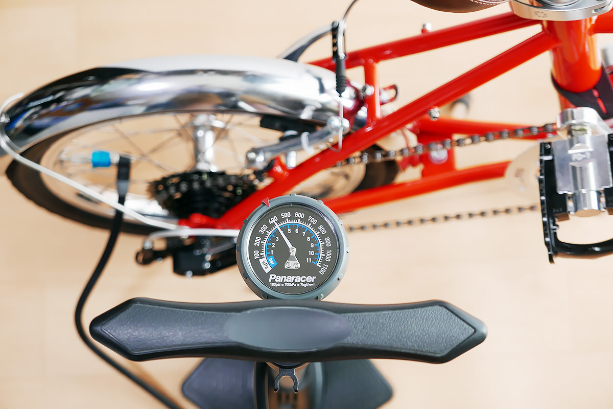 自転車のタイヤに空気圧計付きのフロアポンプ（空気入れ）を接続して、空気を入れる様子。
