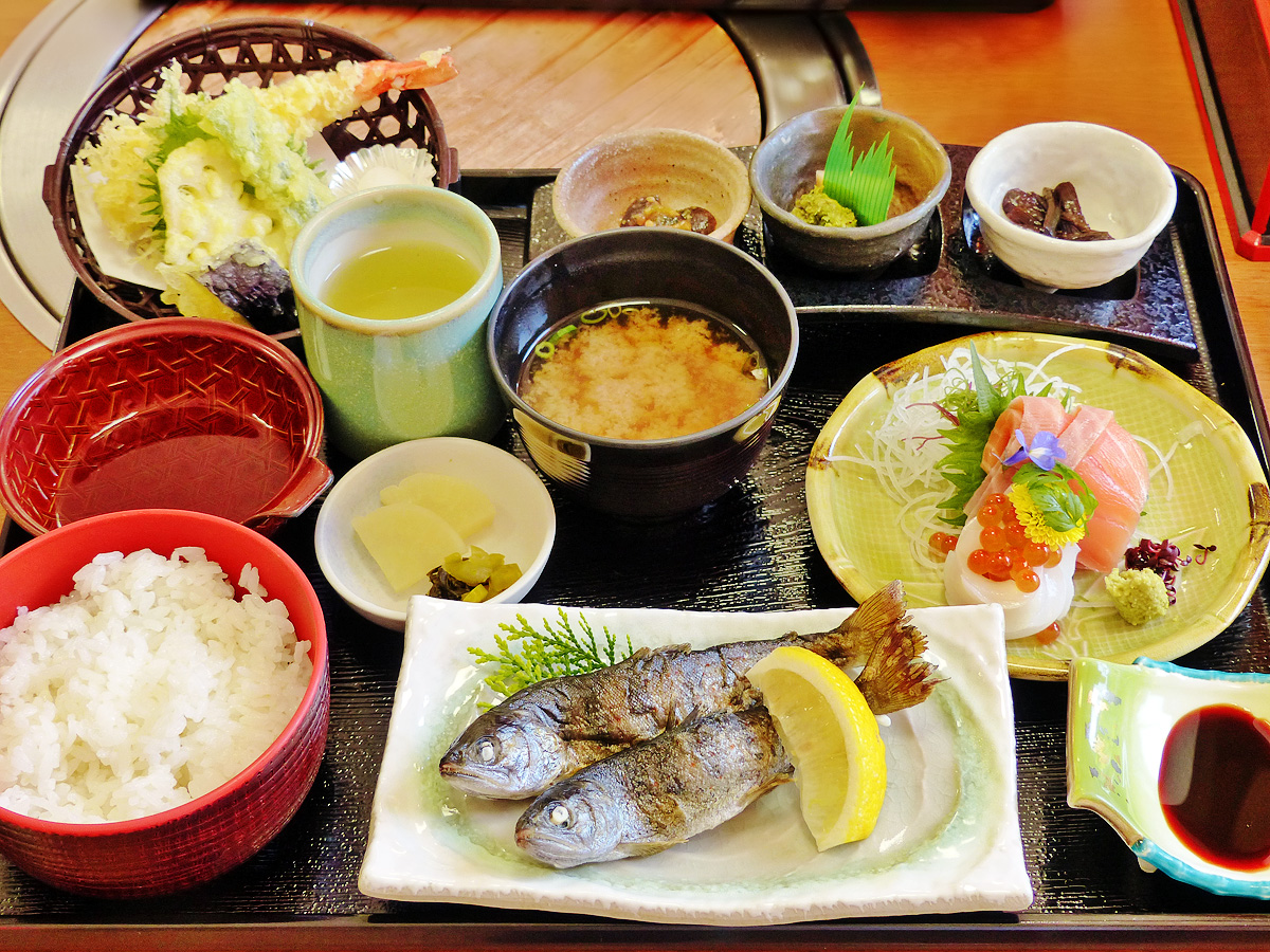 「グリーンエコー笠形」内にあるレストランのお食事「笠形御前」の写真。川魚「アマゴ」の塩焼きと、その他お刺身・天ぷらなど色々なお料理が並んでいる。