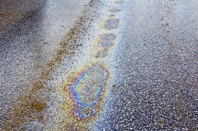 道路が滑りやすくなる原因の一例として、道路上の油膜の写真。雨で濡れたアスファルトに、さらに油が乗っている様子が判る。