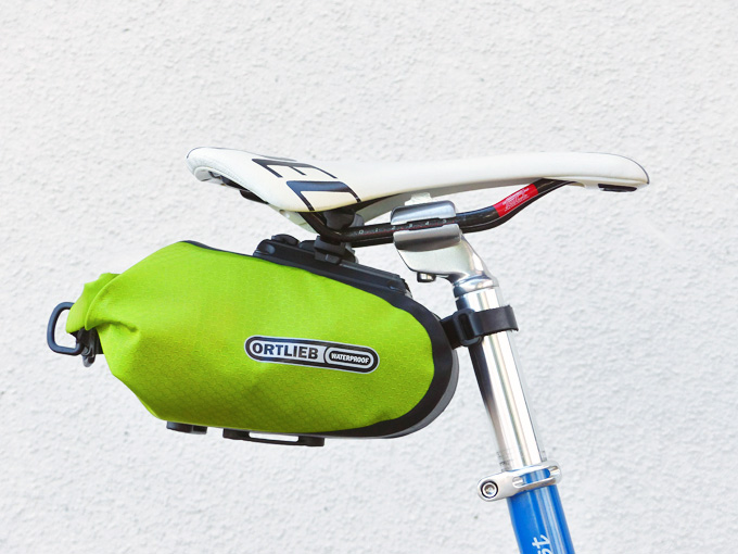 オルトリーブの「サドルバッグM」が、自転車のサドルの下に装着されている様子を横から見た写真。サドルバッグは明るい黄緑色で、「オルトリーブ」のロゴがプリントされている。