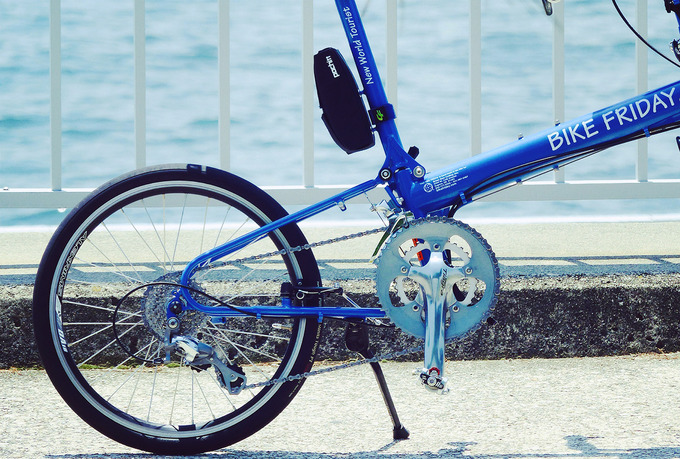 バイクフライデーの自転車「ニューワールドツーリスト」の後ろ半分を写した写真。青いフレームで、銀色の大きなギアが付いている。背景には白いフェンスと青い海が見える。