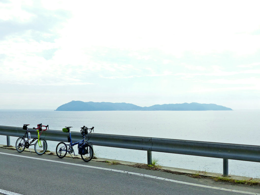高台から海を見下ろす風景。海の向こうには「沼島」が見える。ガードレールの前に2台の自転車、バイクフライデーの折り畳みミニベロ「ニューワールドツーリスト」とミニベロロード「コメットR」が停められている。