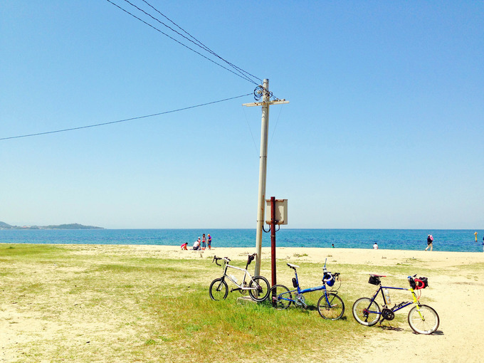 「慶野松原海水浴場」の写真。青い海・白い砂浜が広がる風景の真ん中に、3台のミニベロが停められている写真。