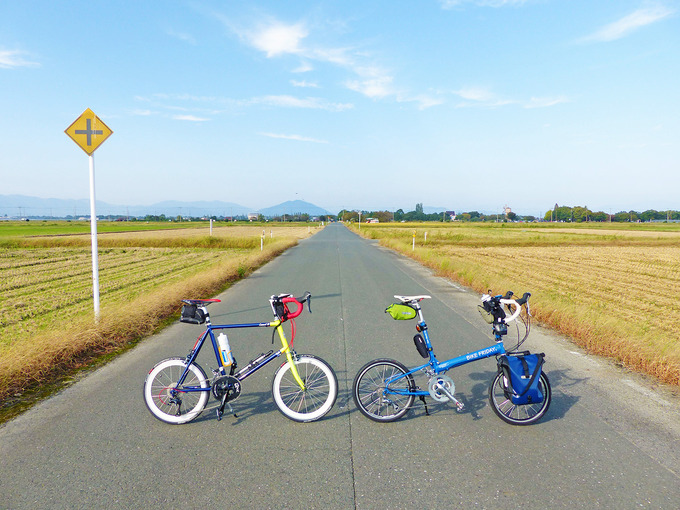 滋賀県高島市の広大な田園風景。収穫を終えた後の田んぼの真ん中に、まっすぐの道路が続いている。道路には2台の自転車、「ニューワールドツーリスト」と「コメットR」が停められている。